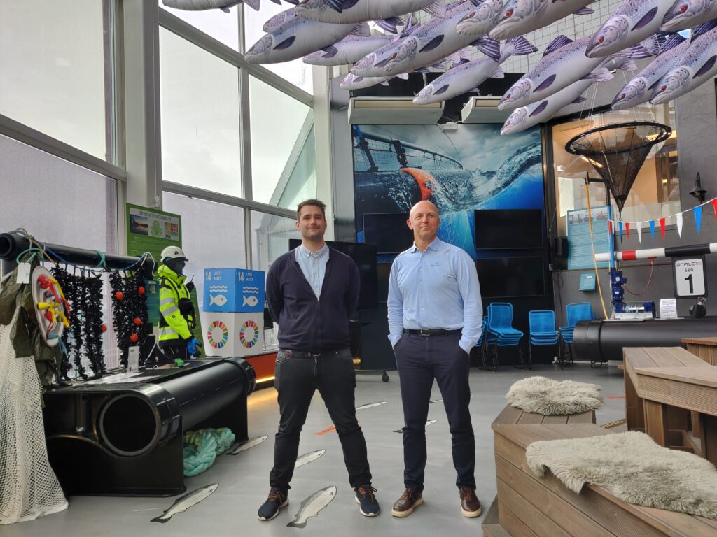 John-Christian Andreassen og Jarle Solemdal står i Salmon Center. Det er utstilt garn og kuber med bærekraftsmål i lokalet. Det er en fiskestim hengende fra taket, og illustrert på gulvet.
