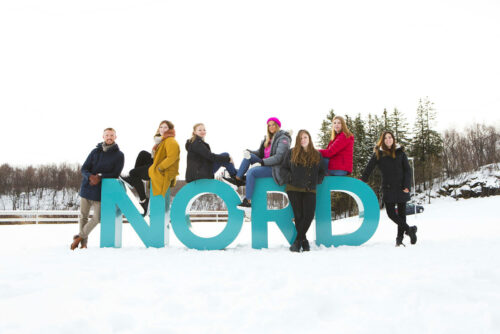 Studenter som sitter på Nord-logoen ute på vinterstid