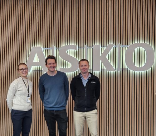 Tre personer står foran en vegg med logo